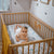 A baby girl with a bow in her looking up at a camera from her cot which has our Eton fitted sheet on it. 