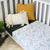 A cot with a Windsor fitted sheet and an Eton Flat sheet on top. There are a white and yellow cushion in the corner of the cot. 