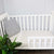 A cot with an Earl Grey sheet set on it which includes a fitted and flat sheet.