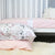 A picture of two pillows in front of a cot with a pink sheet on it. 